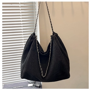 Detail of black canvas tote bag showing metal chain strap and pleated drawstring texture