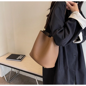 Sac seau en cuir grainé marron avec logo de la marque porté par un mannequin chic