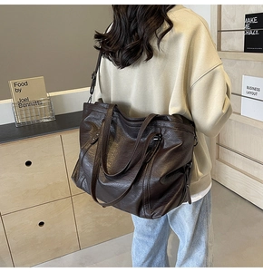 Detail of dark brown vintage oil-wax tote bag with side buckles and glossy leather texture