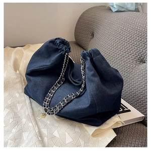 Detail of blue denim tote bag featuring drawstring closure and metal chain strap