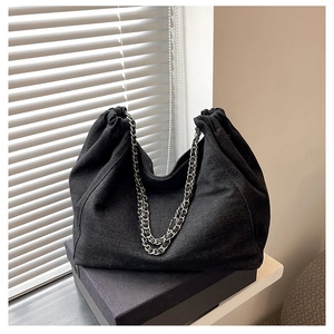 Detail of black denim drawstring bucket bag with silver metal chain shoulder strap