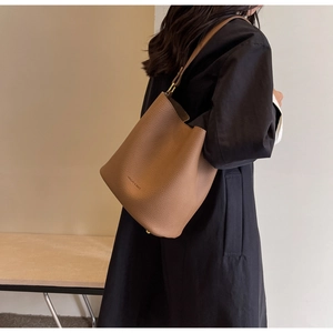 Gros plan sur un sac seau en cuir marron avec l'inscription MACUPE & BAGS porté