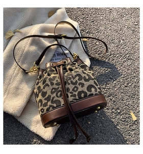 Detailed view of leopard print bucket bag with brown leather trim and golden hardware