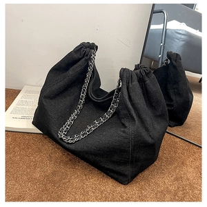 Detail showing black denim hobo bag with silver chain strap on a brown carpet