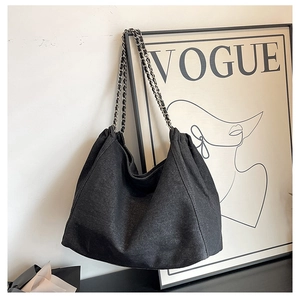 Detail of black denim tote bag with silver chain strap and minimalist pleated design