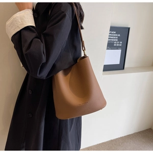 Détail du sac seau en cuir marron avec motif litchi, logo embossé et bandoulière réglable