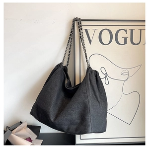 Detail of black denim tote bag with chic woven metal chain strap and fabric texture