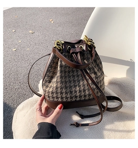 Close-up of retro houndstooth bucket bag with dark brown leather drawstrings and gold hardware