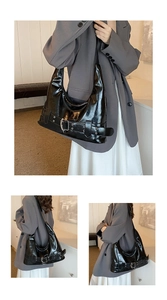 Detail of glossy black hobo bag featuring wide decorative belts and metal buckles