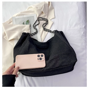 Close-up of black denim hobo bag with woven chain strap and smartphone for size reference