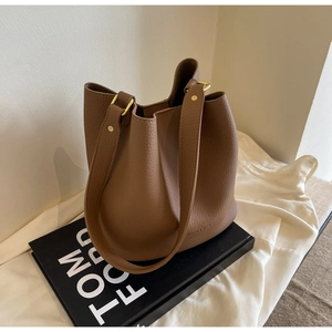 Détail du sac seau en cuir grainé marron avec finitions dorées et large bandoulière souple