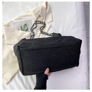 Detail view of durable black denim tote bag featuring silver chain woven leather shoulder strap