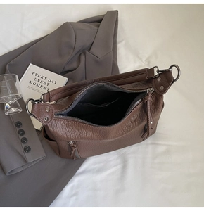 Detailed close-up of brown litchi textured leather tote bag with tassels and silver zippers