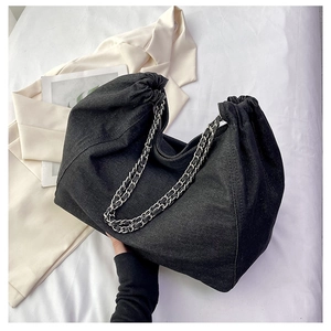 Detail view of black denim cloud bag with metal chain strap and pleated texture on white bedding