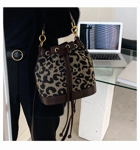 Detailed macro view of leopard print canvas bucket bag with brown leather trim and golden hardware