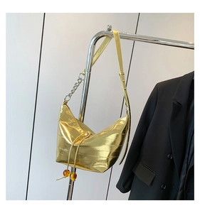 Detalle de bolso de hombro dorado texturizado con cadena plateada y cordón con cuenta ámbar