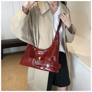 Close-up of wine red patent leather shoulder bag with silver buckle and belt detail