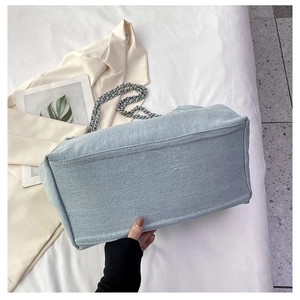 Detail view of denim tote bag with chain strap and reinforced stitching on wide bottom