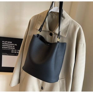 Détail du sac seau noir avec texture litchi et finitions dorées sur un trench beige