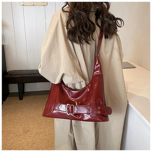 Close-up of a burgundy patent leather shoulder bag with a large metallic belt buckle
