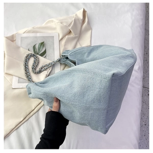 Detail of light blue denim hobo bag with silver chain strap on white fabric background
