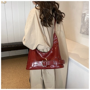 Detail view of deep red patent leather shoulder bag with a large metallic buckle