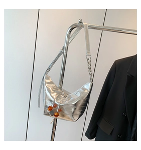 Detalle de bolso bandolera plateado metalizado con pliegues y cordón de perlas ámbar