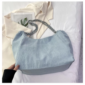 Detail of light blue denim tote bag with silver chain strap on white fabric background