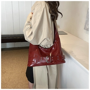Close-up of shiny dark red patent leather shoulder bag with metallic buckle detail