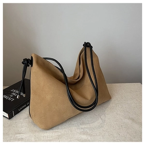 Détail du sac hobo en daim camel avec bandoulière en cuir noir nouée sur une table