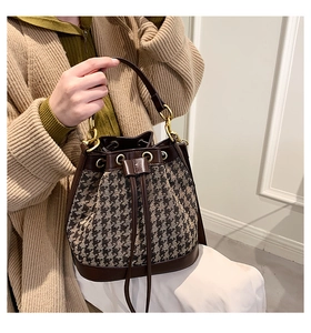 Detail of houndstooth bucket bag with brown leather trim and gold drawstring eyelets
