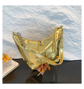 Detalle del bolso medialuna dorado metalizado con cadena y colgantes rojos