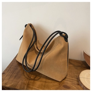 Détail du sac fourre-tout en daim marron avec anses nouées noires sur table en bois