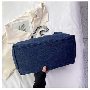 Detail view of large denim tote bag with silver chain strap and wide bottom structure