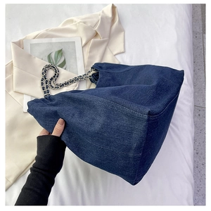 Detailed close-up of large denim tote bag with silver chain strap and washed texture