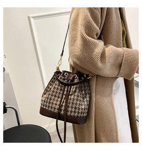 Detail of a brown houndstooth bucket bag with leather trim and drawstring closure