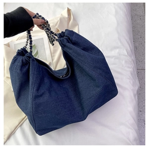 Detail of blue denim tote bag featuring ruched opening and woven metal chain strap