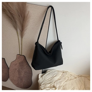 Détail du sac à bandoulière noir minimaliste montrant la décoration de nœud et la texture mate