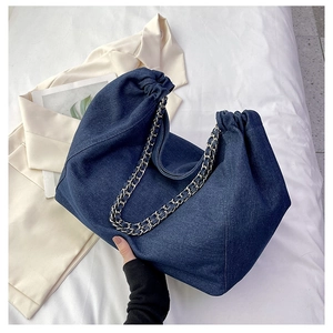 Detail of the large denim tote bag featuring a metal chain strap and pleated edges