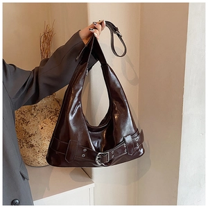 Detail of a dark brown glossy hobo bag with retro belt buckles and metal eyelets