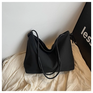 Détail d'un sac cabas noir minimaliste avec bandoulière nouée sur fond en tissu blanc