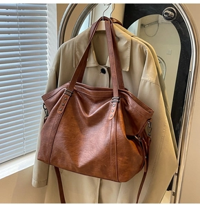 Detail of vintage brown tote bag with star rivets hanging on a beige trench coat