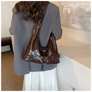 Detail of dark brown glossy shoulder bag with metal buckles on grey suit and white dress