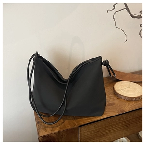 Détail d'un sac HOBO noir minimaliste avec nœuds décoratifs sur surface en bois