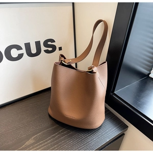 Détail de sac seau marron en cuir avec grain lychee et accessoires métalliques dorés chic