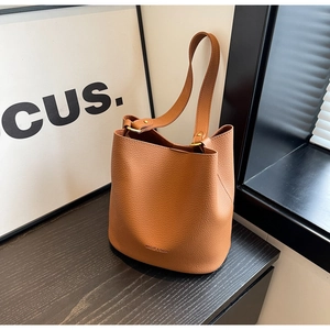 Détail d'un sac seau en cuir grainé marron avec finitions dorées et logo de la marque