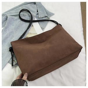 Détail du sac fourre-tout marron foncé avec de fines bandoulières noires sur un lit