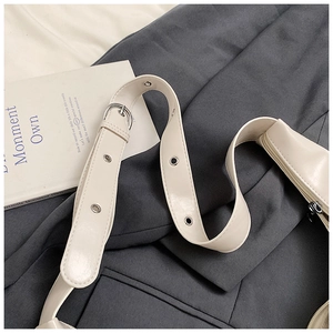 Close-up of white leather shoulder bag featuring silver metal eyelets on a wide strap