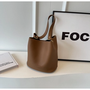 Détail d'un sac seau en cuir marron à motif lychee avec un design de bandoulière minimaliste