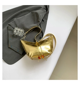 Detalle de bolso de hombro creciente dorado en cuero sintético con dije de cuenta de ámbar